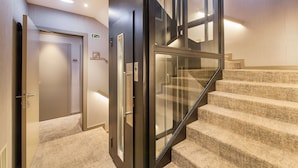 Un interior de hotel moderno con una escalera alfombrada, un ascensor de cristal y una pared de madera.