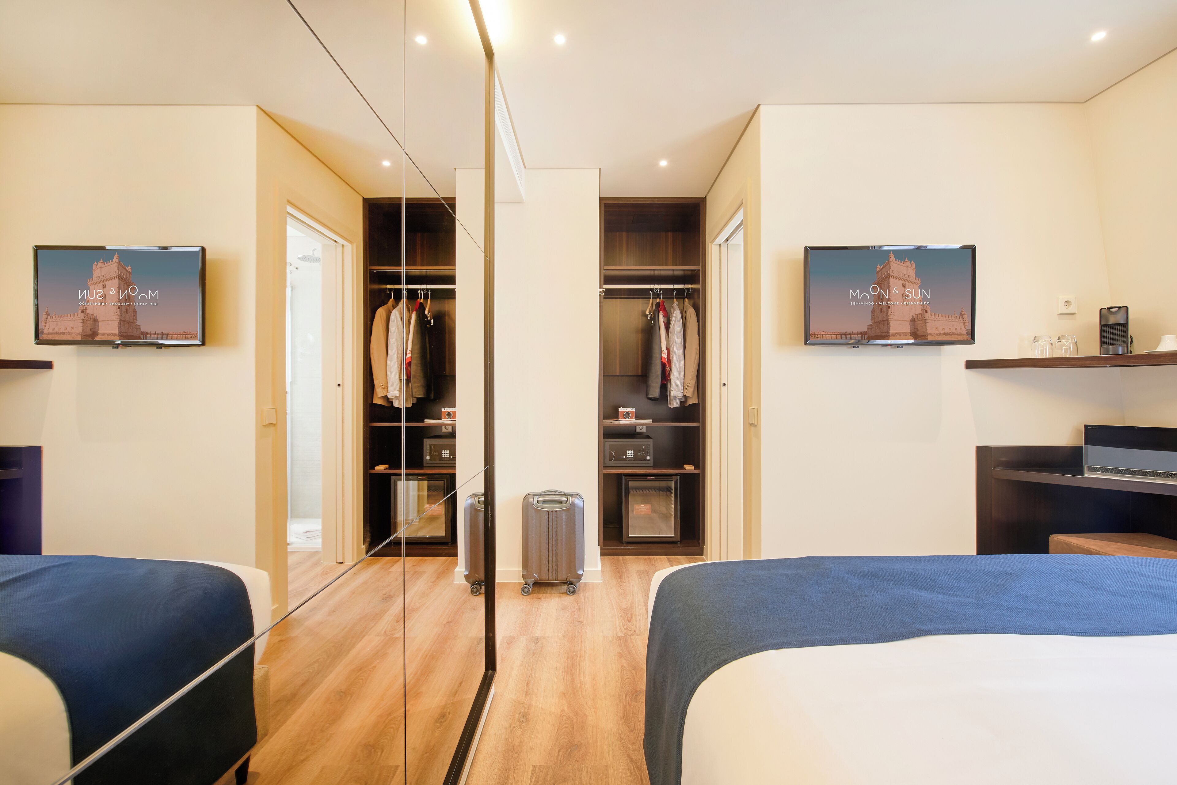 A hotel room with two beds, a wardrobe, a mirror, and a television displaying a sunset view.