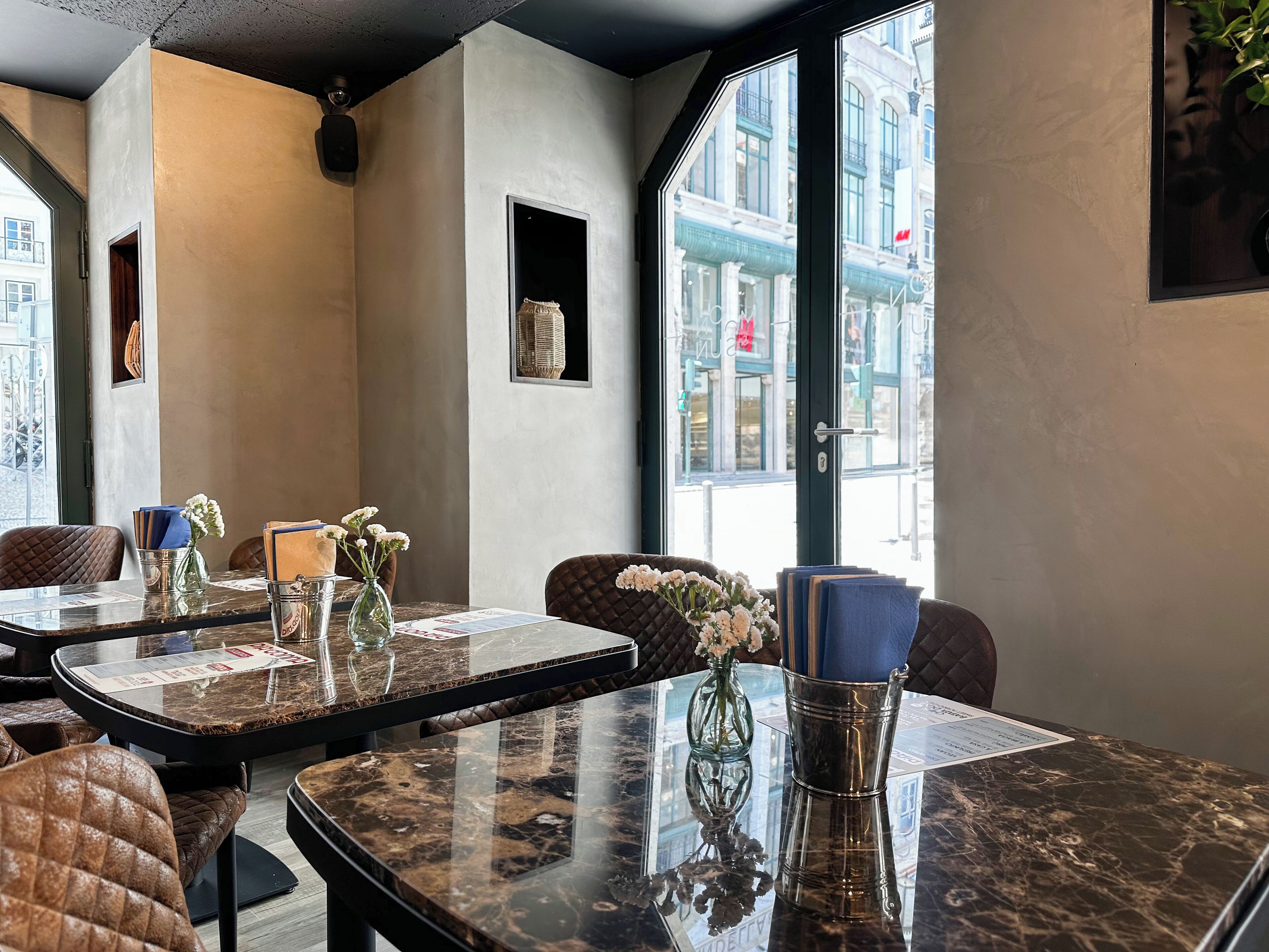 A modern dining area with marble tables, cushioned chairs, and a view of the city through large windows.
