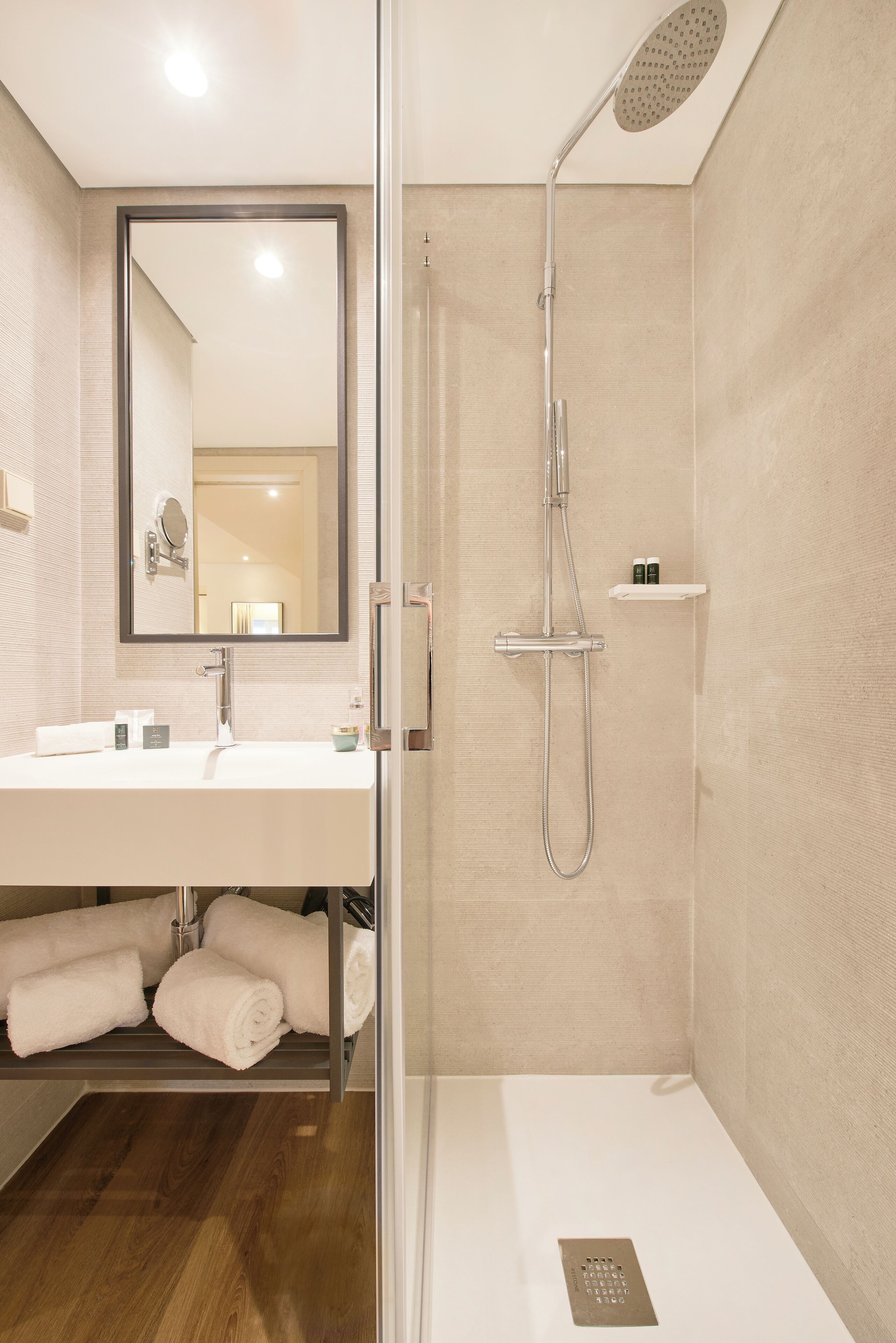 Un baño moderno con ducha de vidrio, un espejo grande y un tocador blanco con toallas.