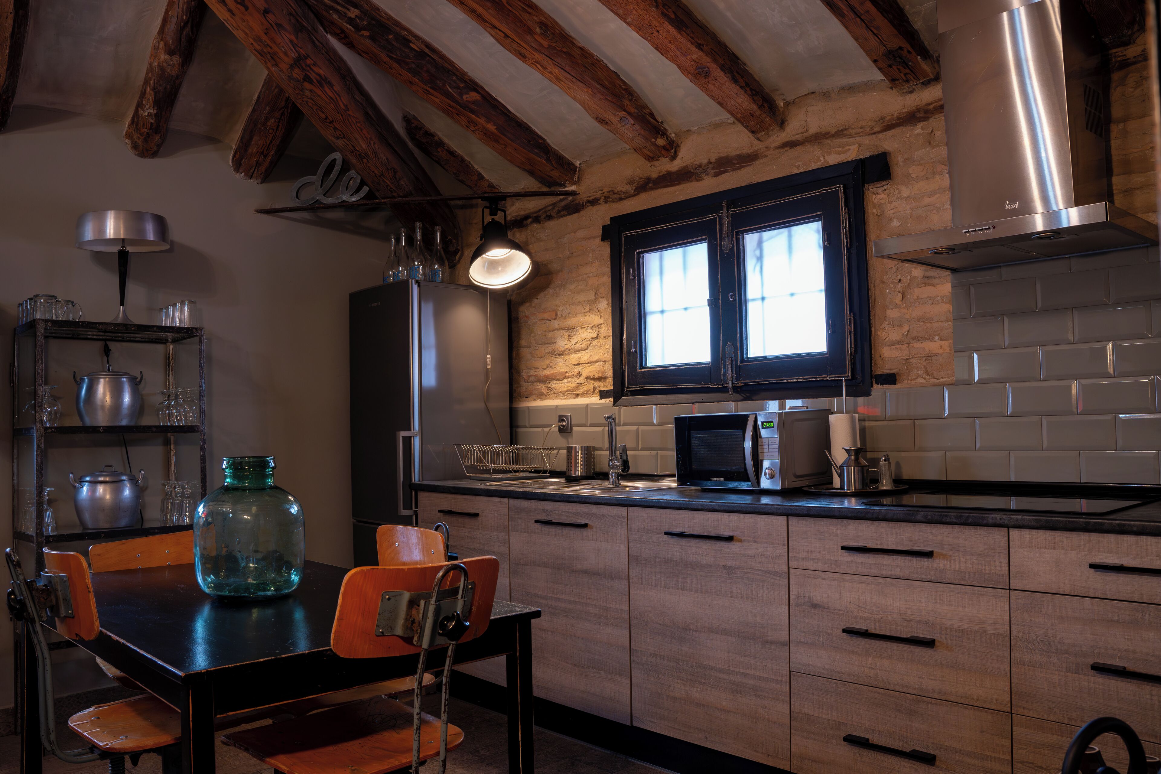 A kitchen with wooden beams, a window, a microwave, and a table with chairs.