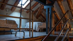 A loft bedroom with a high ceiling, exposed wooden beams, a skylight, and a metal ladder leading to a lofted bed.