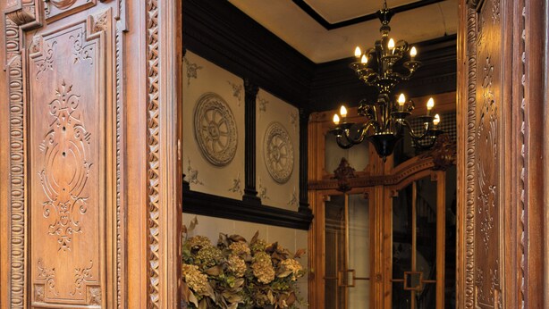 A checkered floor, wooden doors, a chandelier, and a vase with flowers.