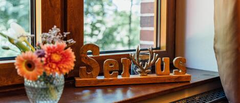 A wooden sign with the word "Serious" on a window sill, next to a vase with flowers.