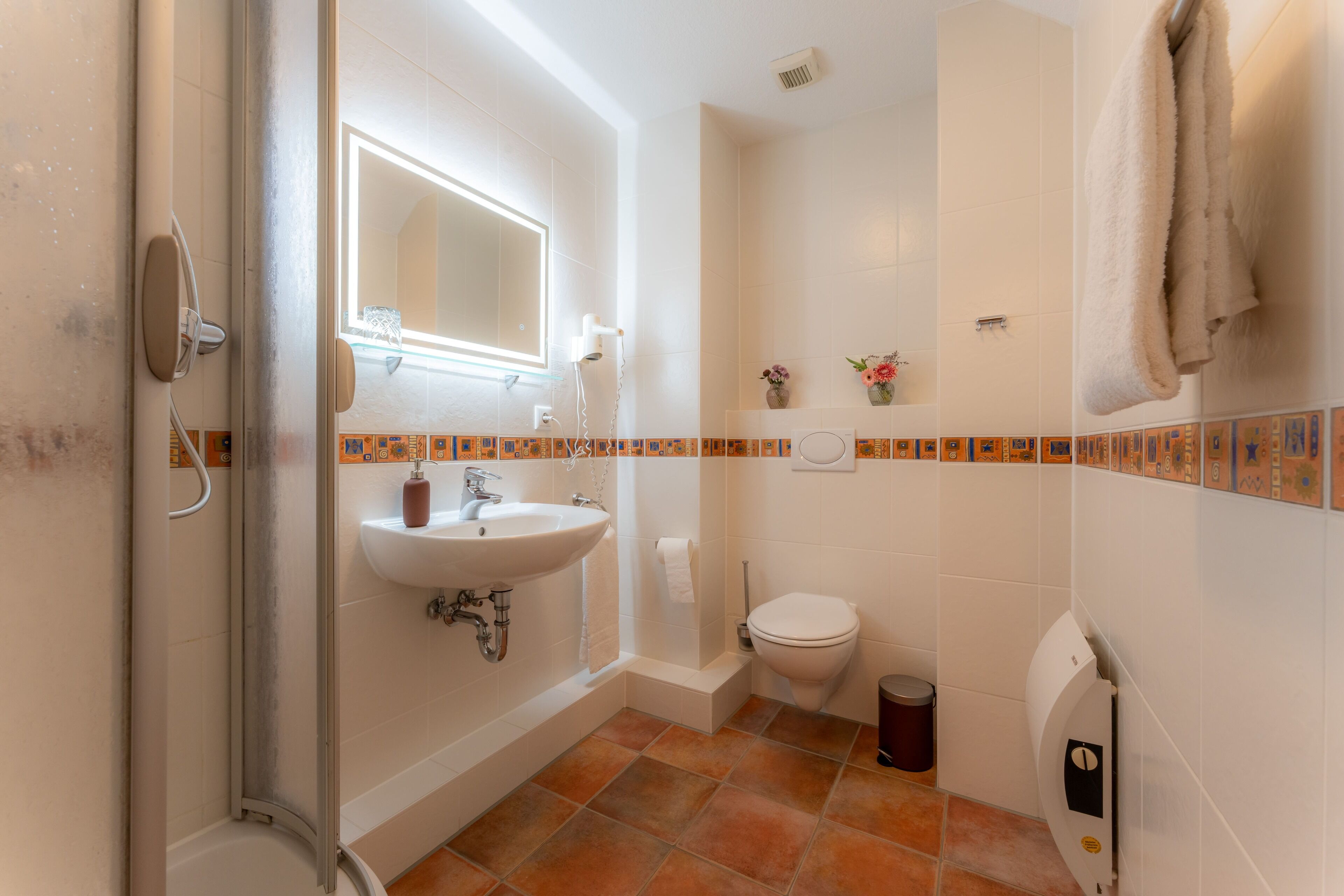 Baño con ducha, lavamanos, inodoro y toallero.