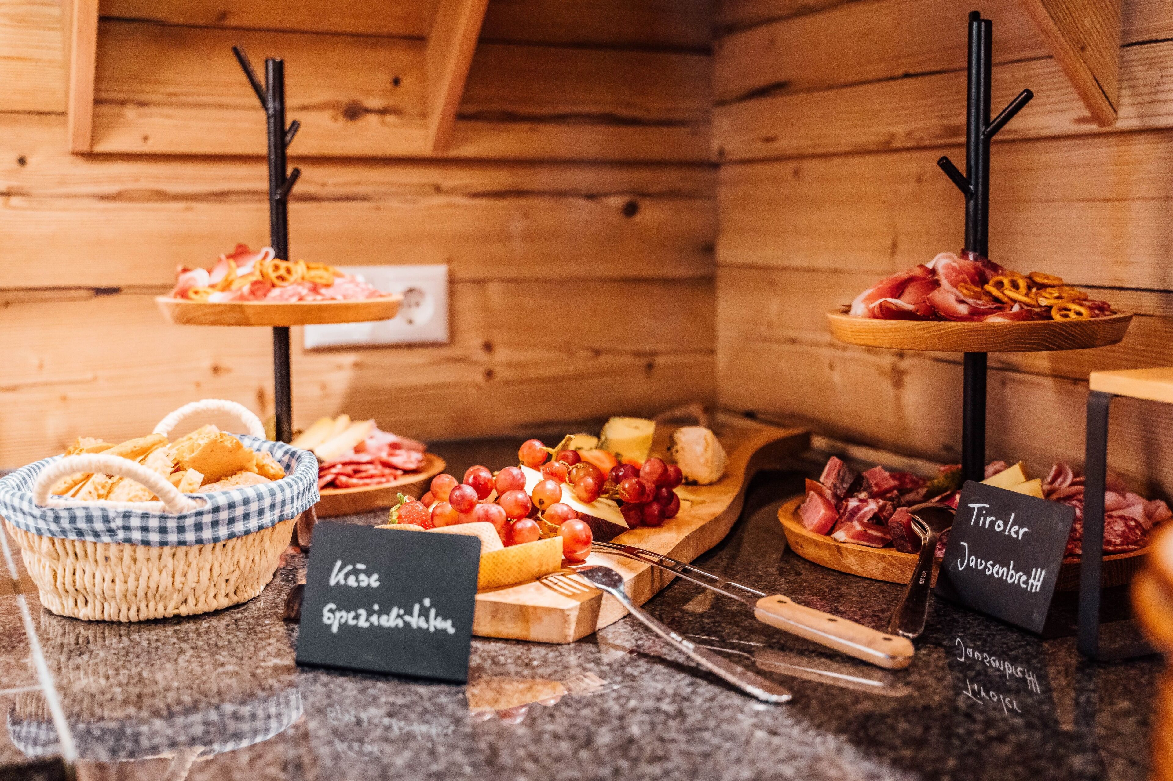 Interior de una cabaña de madera con una mesa de buffet que exhibe quesos, carnes y pan.