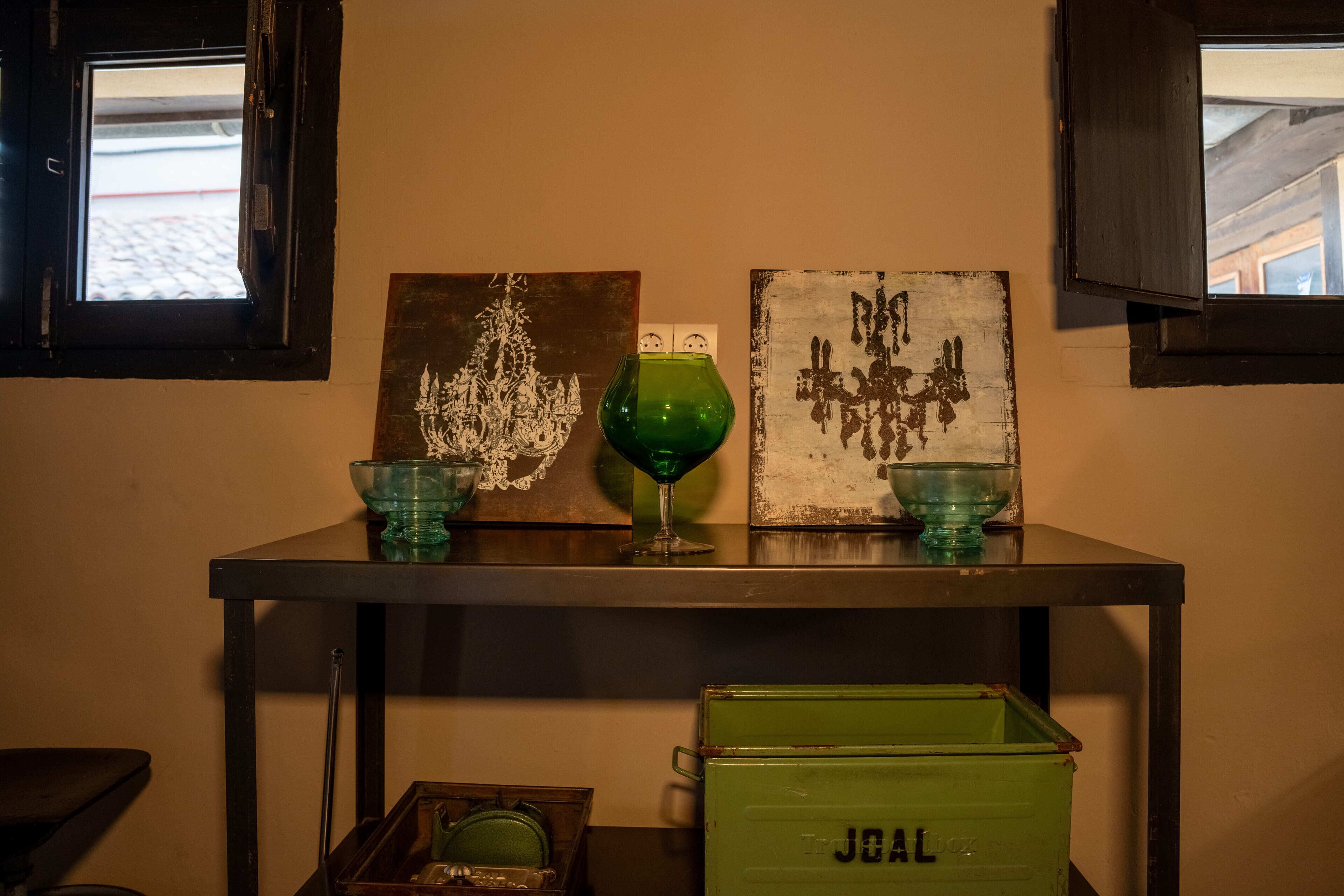 Una mesa con tres jarrones de vidrio, dos obras de arte enmarcadas y un caja verde de almacenamiento.