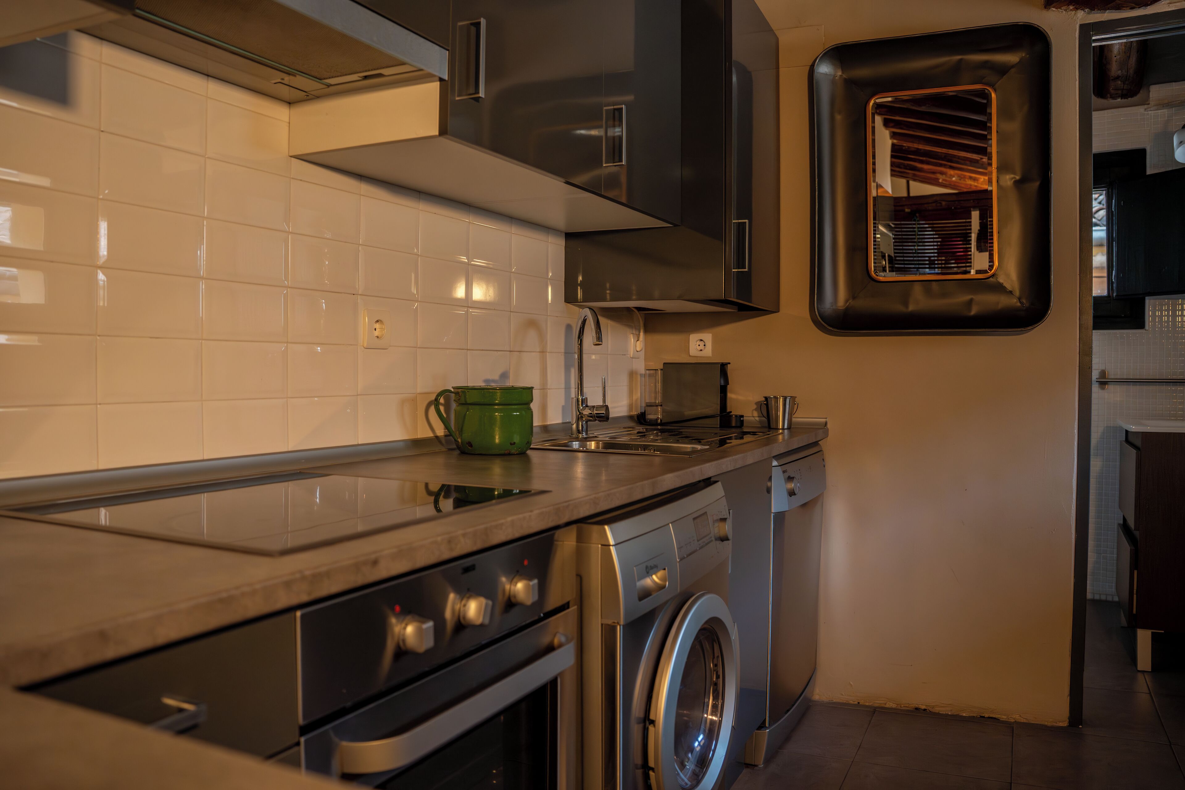 A modern kitchen with a stainless steel oven, a built-in washing machine, and a small window with a view of the interior.