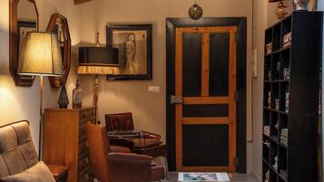 A cozy living room with a wooden cabinet, a leather armchair, a table with books, a lamp, and a door with a glass panel.