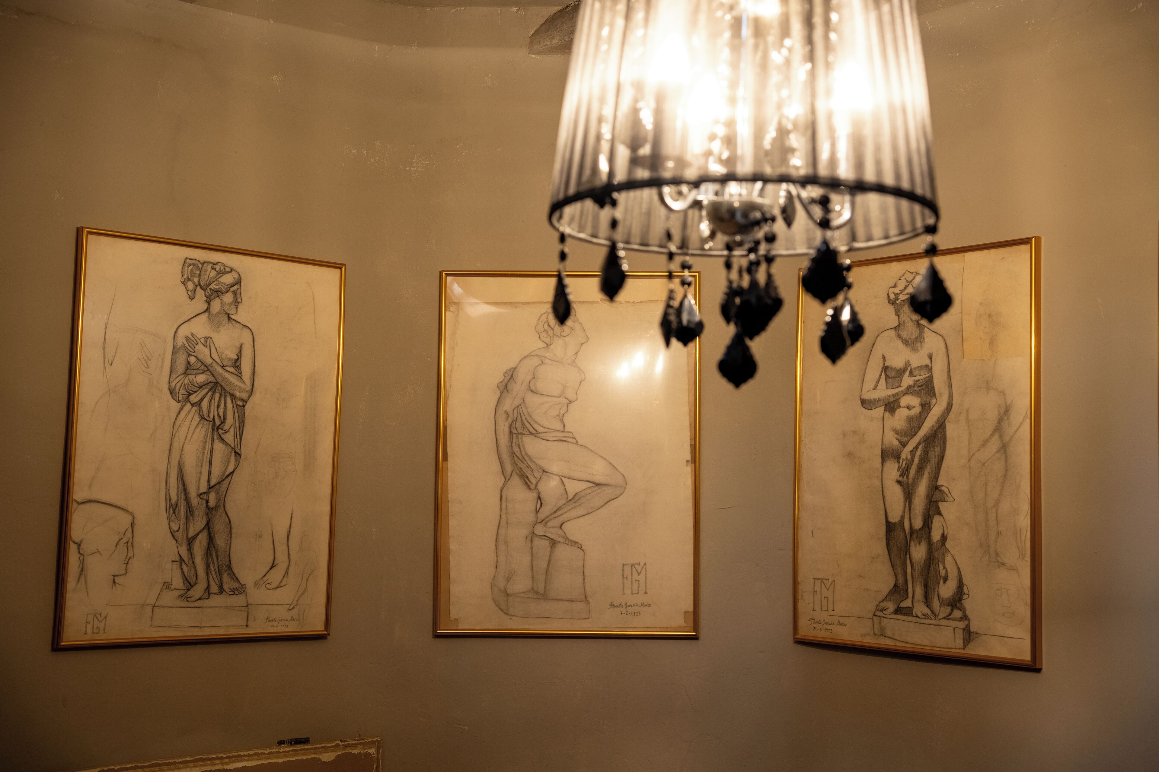 Three framed sketches of figures on a wall, with a chandelier above.