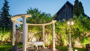 A garden patio with a pergola, a table set for dining, and a rustic building in the background.