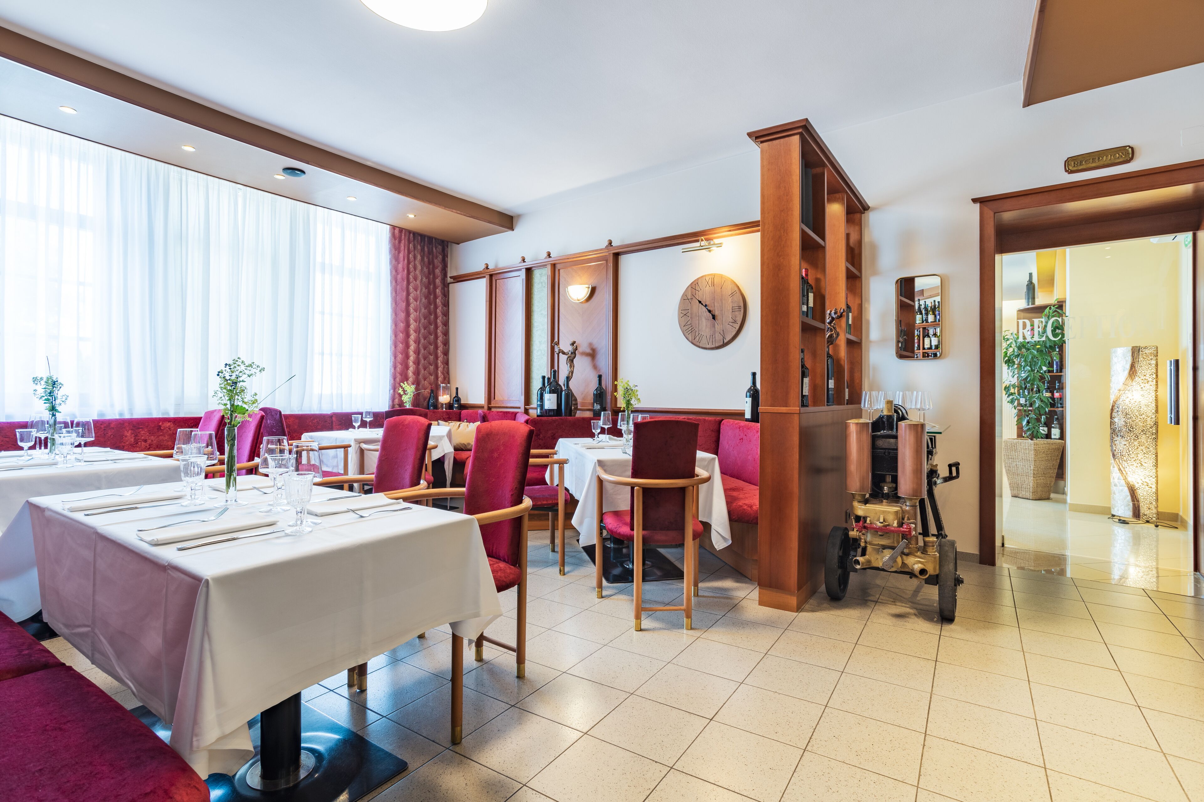 A restaurant with tables set for dining, red upholstered chairs, and a wooden bar area.