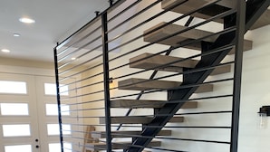 Una scala moderna con ringhiera in metallo, gradini in legno e una porta in vetro sullo sfondo.