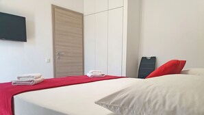 Ein ordentlich bezogenes Bett mit weißer und roter Bettwäsche, eine geschlossene Holztür und ein an der Wand befestigter Flachbildfernseher.