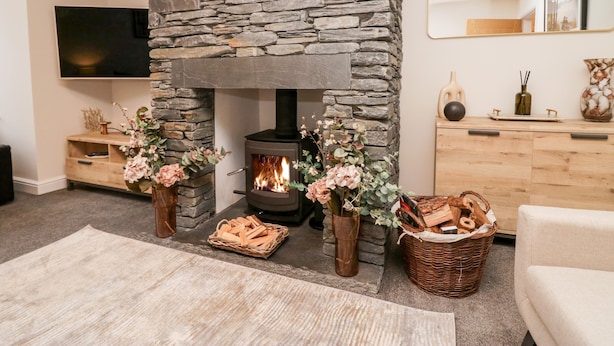 A cozy living room with a stone fireplace, a flat-screen TV, and a wooden cabinet with decorative items. - Rose House (Windermere)