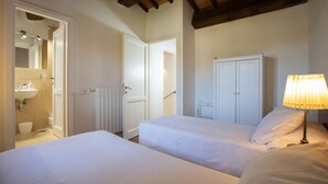 A bedroom with two beds, a bathroom with a mirror, and a wardrobe. - Sweet country home (Montorgiali)