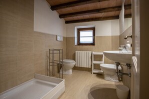 A bathroom with a bathtub, two toilets, a window, and a sink. - Sweet country home (Montorgiali)