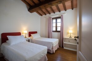 A room with two beds, wooden flooring, a window with curtains, and a door with a handle. - Sweet country home (Montorgiali)