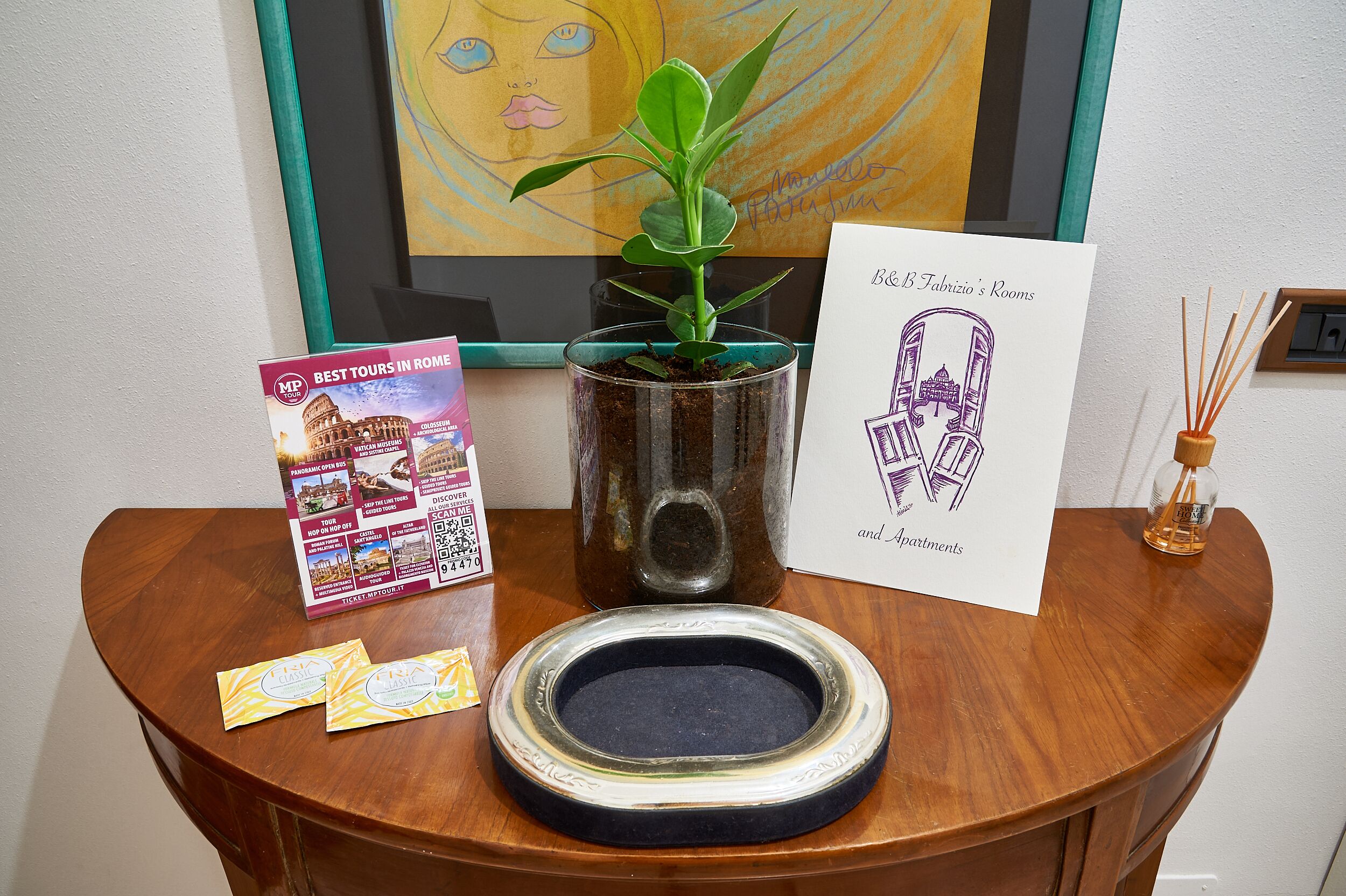 A wooden table with a potted plant, a framed drawing, a brochure, and a small incense burner.