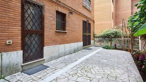 A brick building with a stone-paved courtyard, metal gates, and a small garden with plants and flowers. - Anastasio II apartment  (Rome)