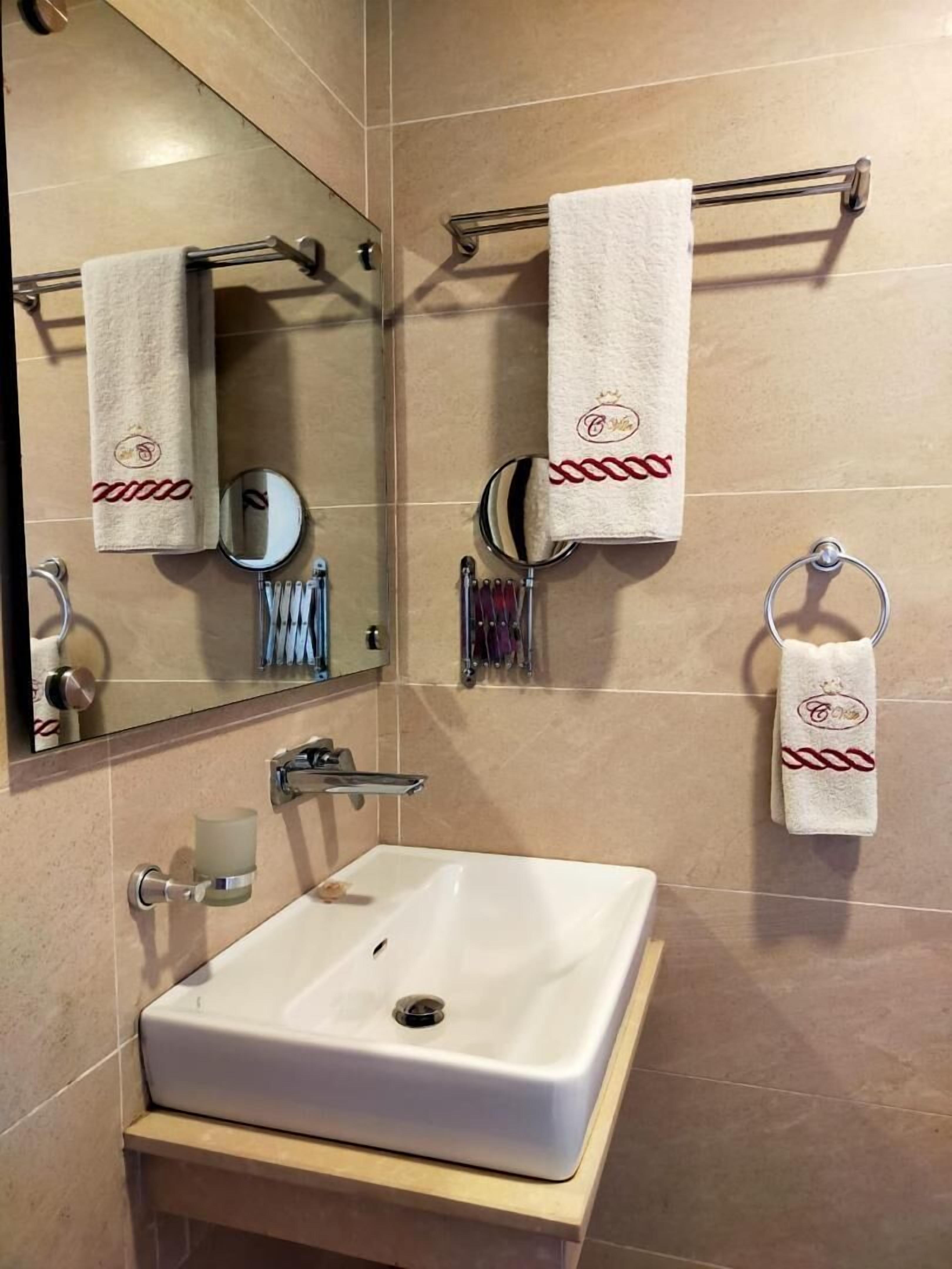 A bathroom with a white sink, two towel racks with towels, a mirror, and a soap dispenser.