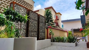 A courtyard with a stone wall, potted plants, and a building with a red staircase. - Catherine Villa (Lagos)