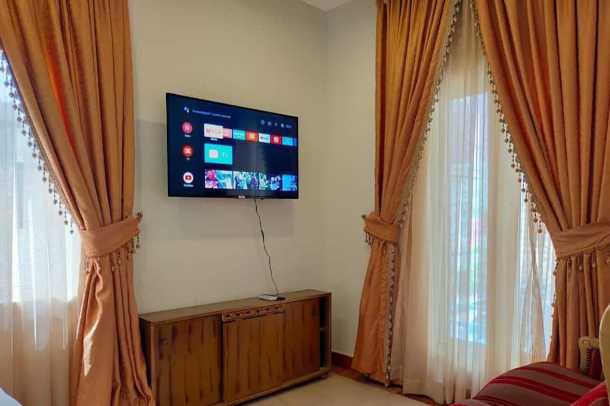 A living room with a flat-screen TV mounted on the wall, a wooden cabinet, and a striped sofa.