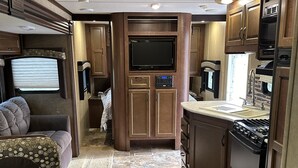 A compact RV kitchen with wooden cabinetry, a built-in TV, and a stove.