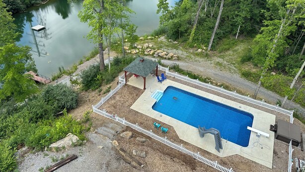 A swimming pool surrounded by a white picket fence, with a gazebo and outdoor seating area.