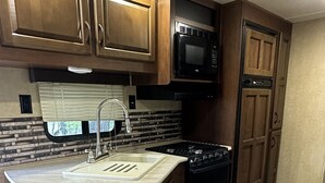A compact kitchen with a built-in stove, a microwave, and a sink with a window above.