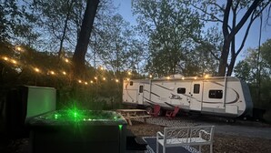 A recreational vehicle (RV) parked in a wooded area with string lights.