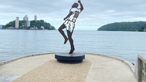 A sculpture of a figure in a dynamic pose on a circular platform with a plaque commemorating Brazil's participation in the 1958-1970 World Fairs.