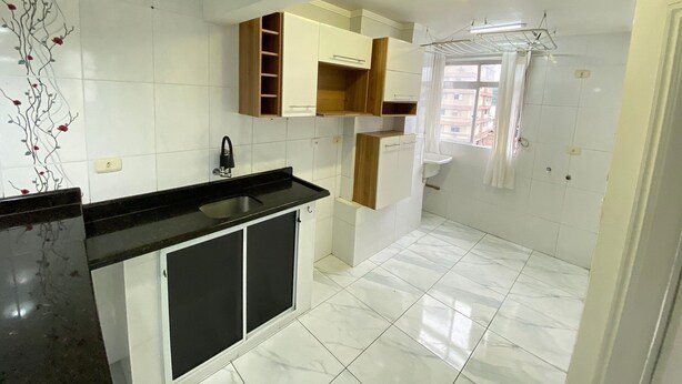 A modern kitchen with white tiles, a black countertop, and wooden cabinets.