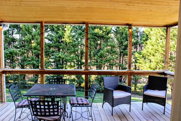 A wooden deck with a table and chairs, overlooking a forested area.