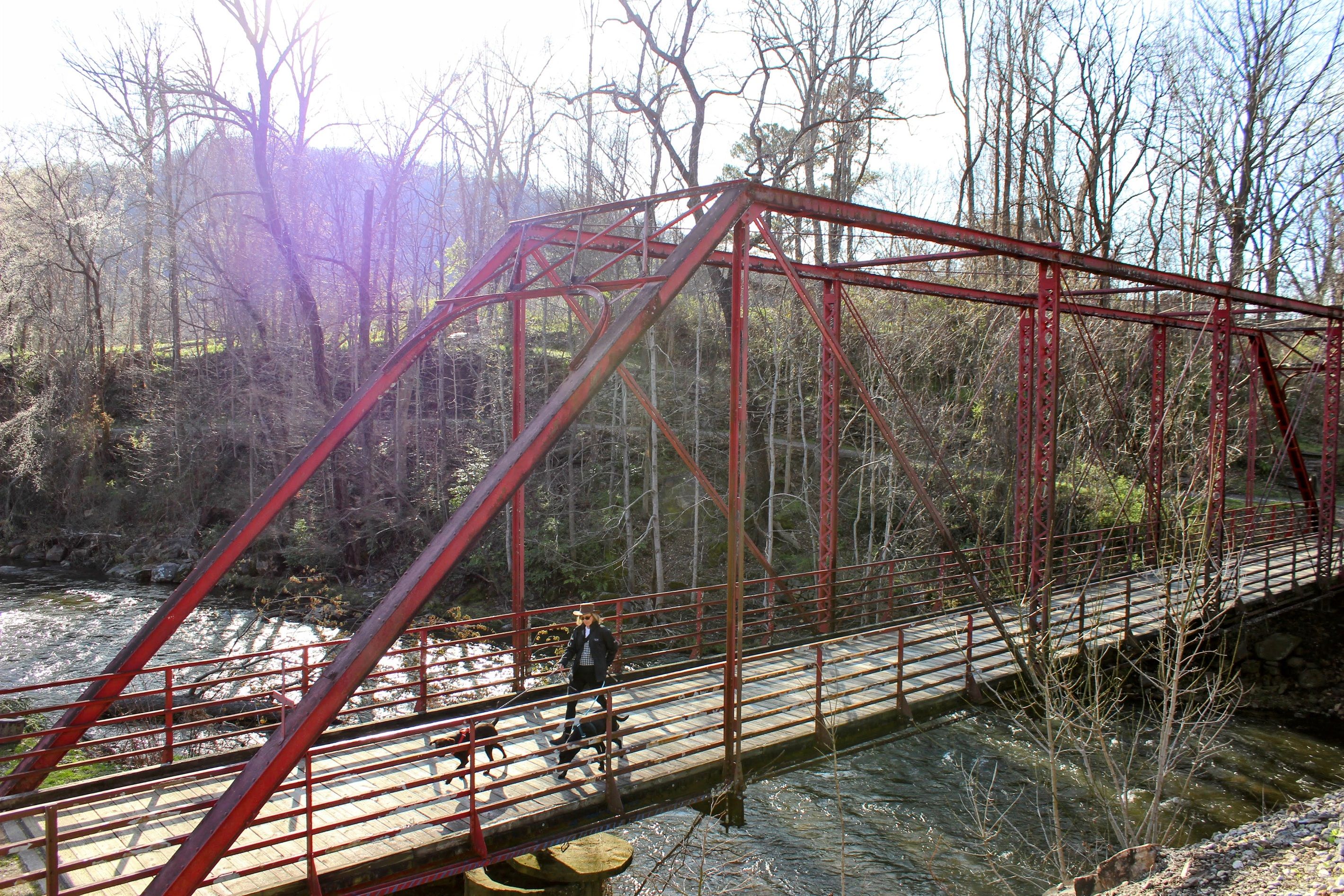 Een rode metalen brug over een rivier, met een persoon die ernaar loopt.