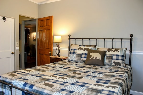 Een slaapkamer met een bed, een houten deur, een nachtkastje met een lamp en een wand met een verlichtingsarmatuur.