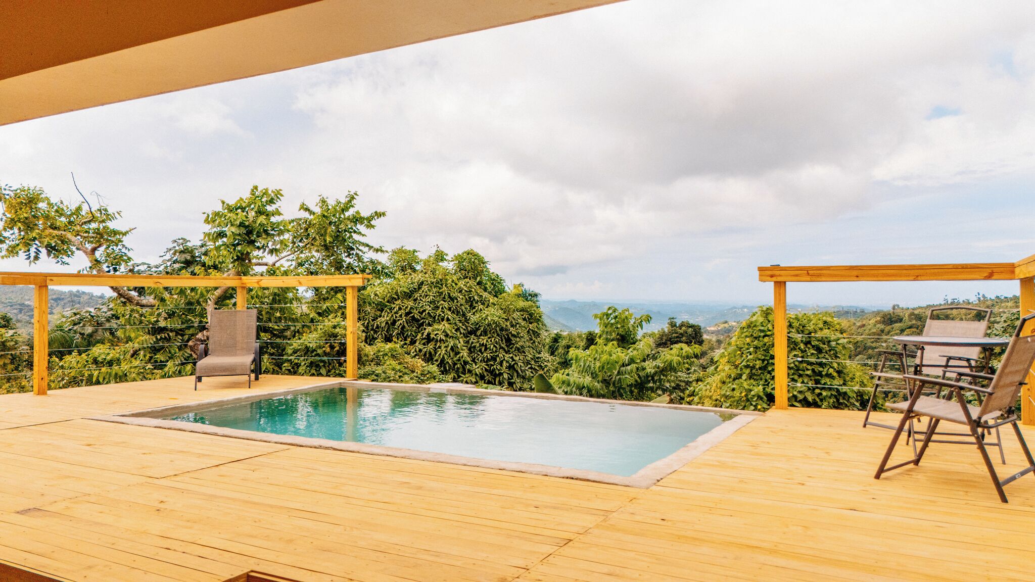 A wooden deck with a pool, two chairs, and a table.