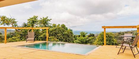 A wooden deck with a pool, two chairs, and a table.