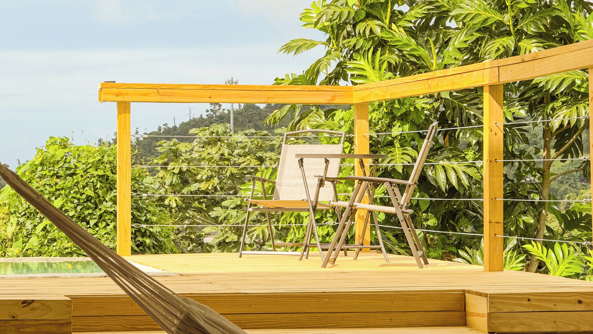 Eine Holzterrasse mit einem Metallstuhl und einer Leiter, umgeben von üppiger Bepflanzung.