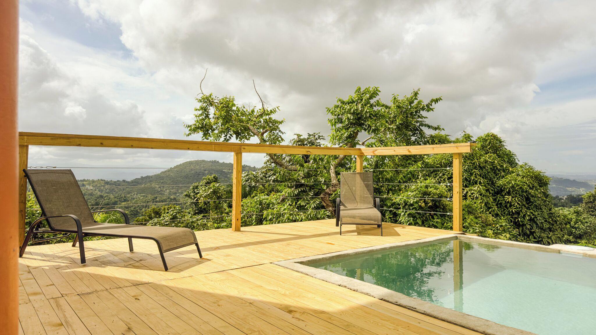 A wooden deck with two lounge chairs and a pool.