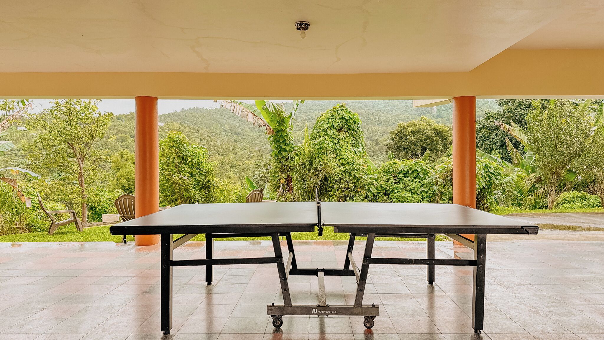 A ping pong table in a covered area with a view of lush greenery and hills.