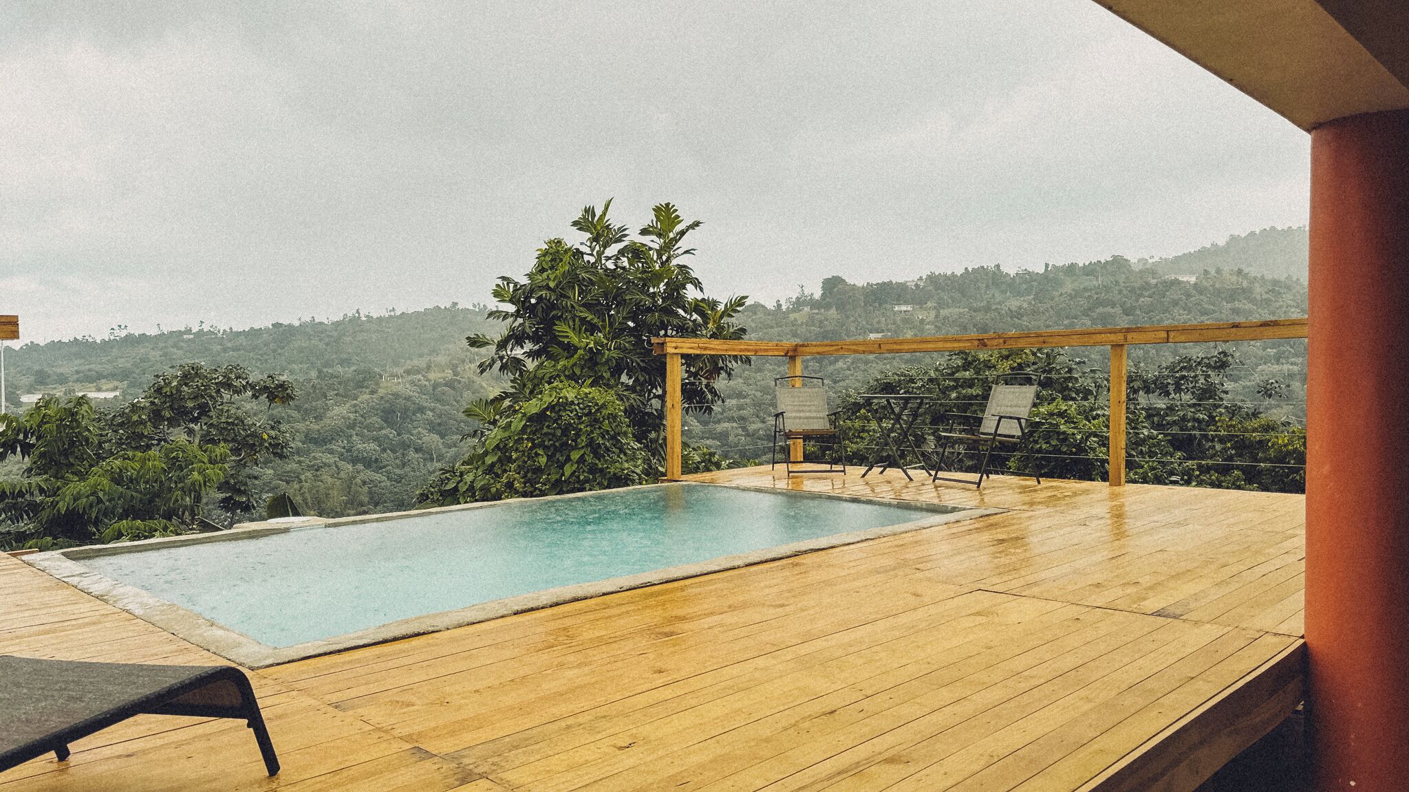 Une terrasse en bois avec une piscine rectangulaire, deux chaises longues et une pergola.
