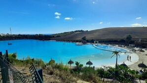 Une grande piscine extérieure avec un espace aménagé comme une plage, des parasols et une colline en arrière-plan.