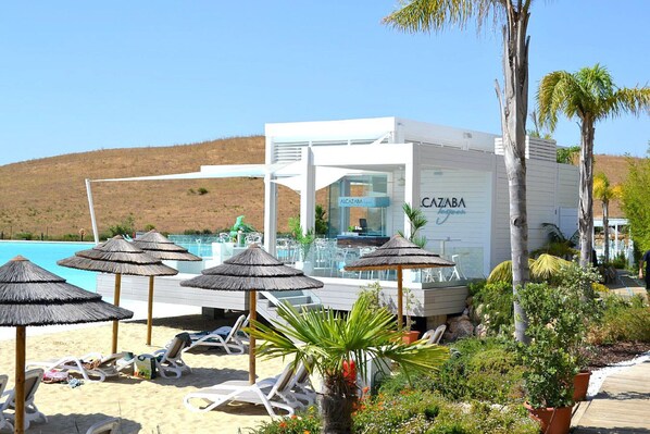 A beachside hotel with a pool, sun loungers, and umbrellas.