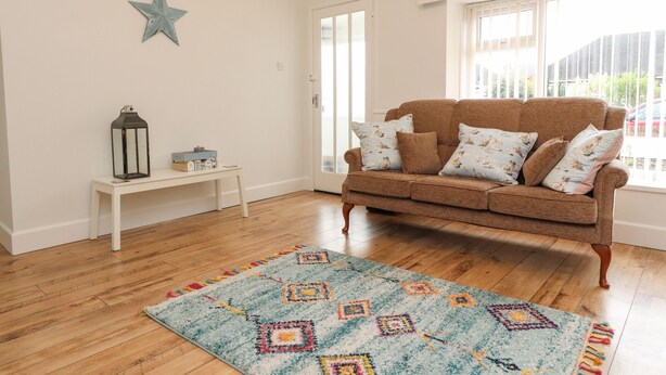 A living room with a brown sofa, patterned cushions, a star decoration, a small table with a lantern, and a colorful rug.
