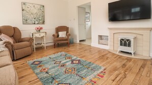 A living room with a brown sofa, a patterned rug, a white fireplace, and a flat-screen TV on the wall.