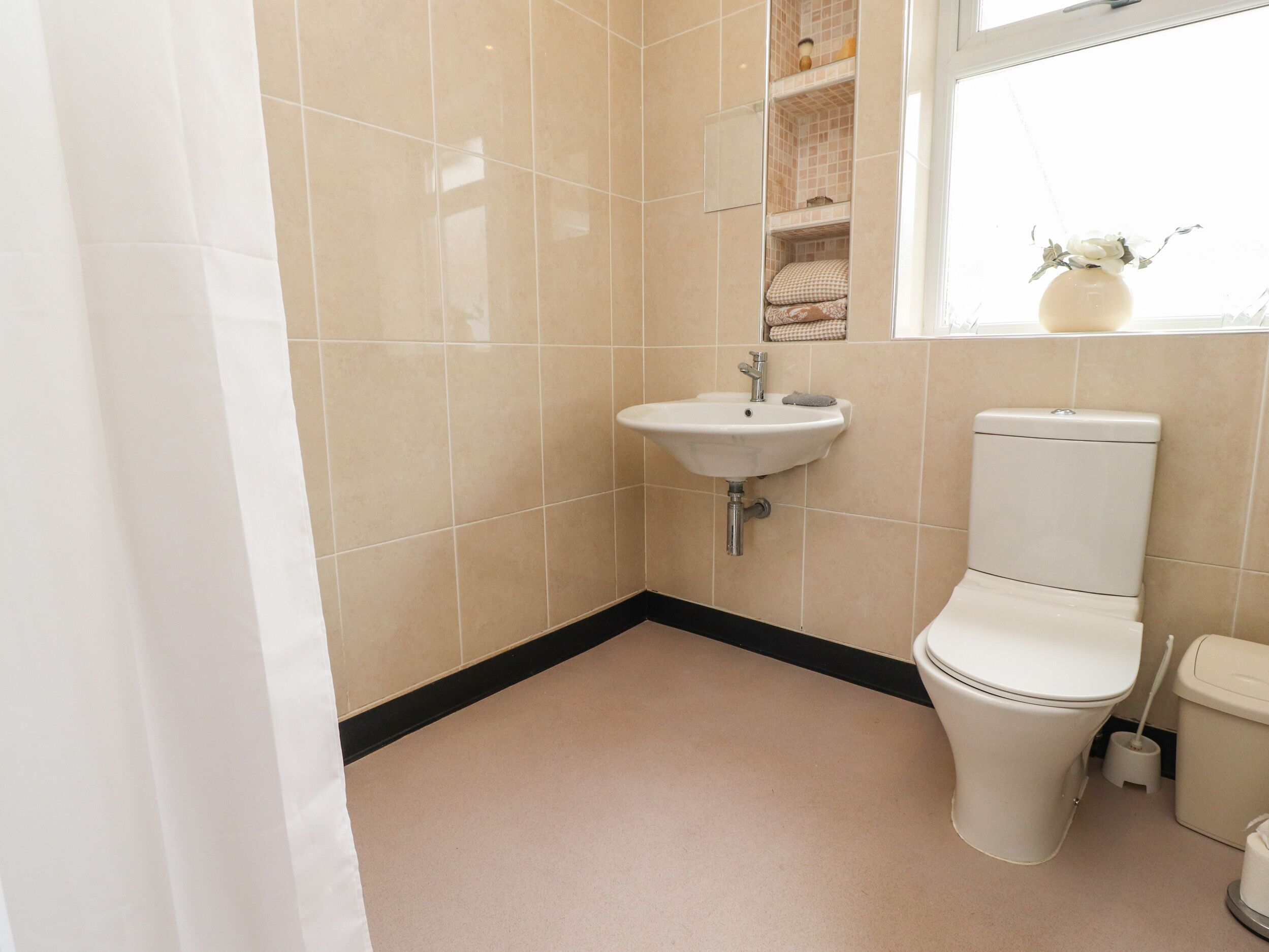 Une salle de bain avec un lavabo blanc, des toilettes et une fenêtre agrémentée d’un vase de fleurs.