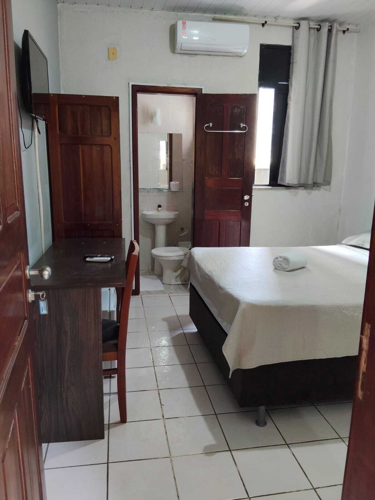 A small, clean room with a bed, a desk, a chair, a toilet, and a sink.