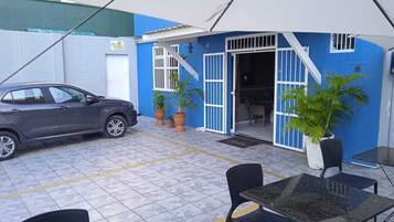 A covered outdoor area with a car parked, potted plants, and a table with chairs.