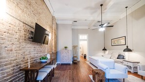 A modern living room with a brick wall, wooden flooring, a dining area with a table and chairs, and a white sofa set. - Experience Mississippi Art at 'The Artistry' (Laurel)
